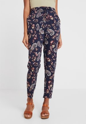 Navy pants with pink, cream, and purple floral and paisley pattern, mid-rise waist, tapered legs, worn with tan heeled sandals.