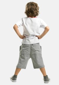 Biała koszulka z krótkim rękawem i czerwonym kołnierzykiem, szare spodenki do kolan oraz szare wysokie trampki z sznurowadłami, widok z tyłu.