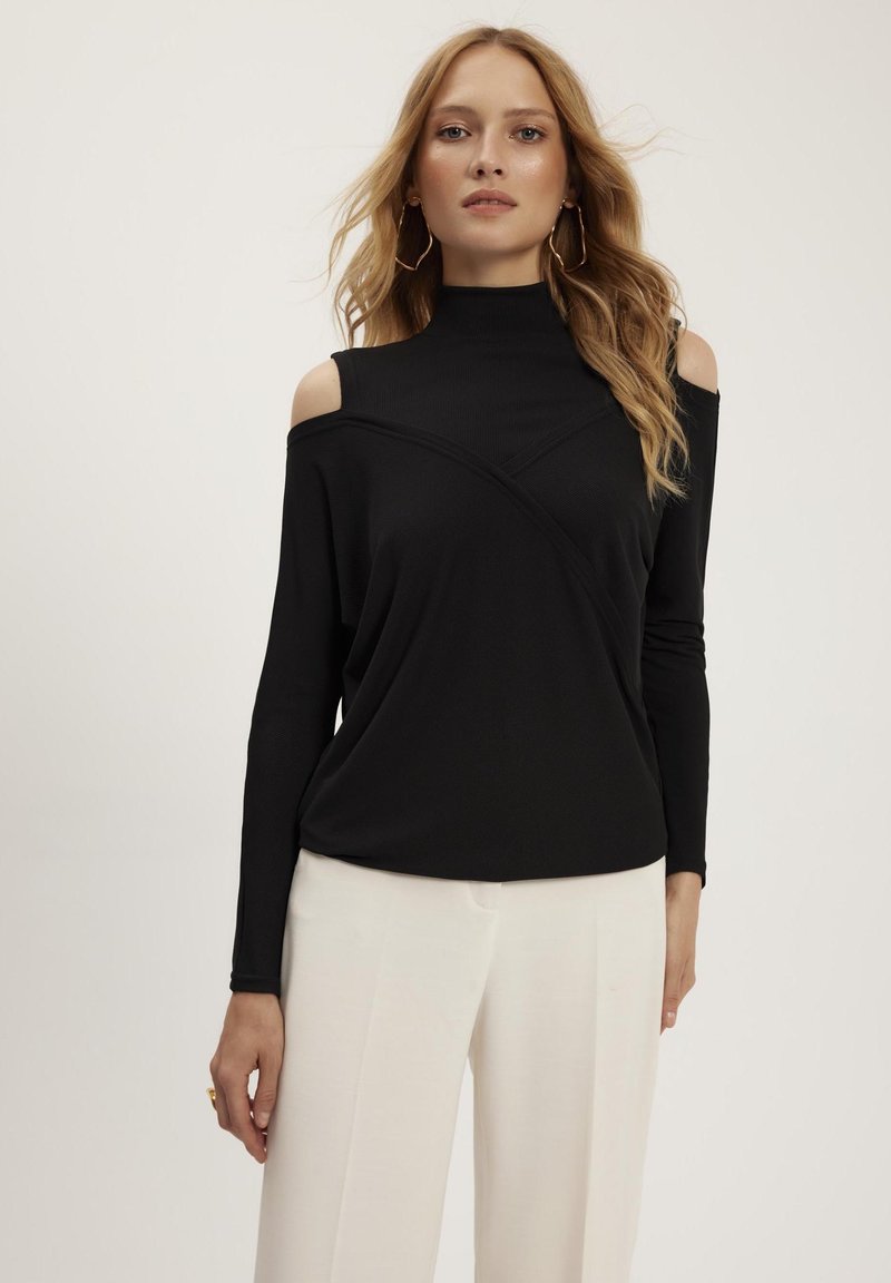 Czarny longsleeve z dekoltem w łódkę i otwartymi ramionami, wykonany z teksturowanej tkaniny z ukośnym szwem. W połączeniu z białymi spodniami.