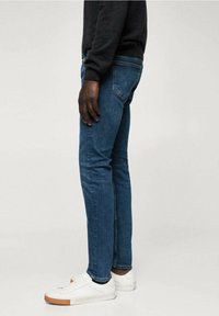 Siniset farkut slim fit -mallissa, joissa on sileä pinta, viiden taskun tyyli ja valkoisten lenkkareiden kanssa yhdistettynä.