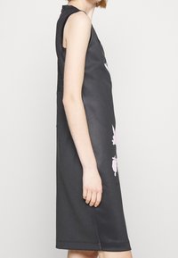 Černé bezrukávové šaty s volným střihem, s růžovými květinovými potisky na přední straně a síťovanou výstuží na zadní straně. Hladký povrch.