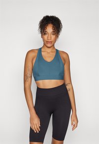 Teal sportsbh med ribbet tekstur og brede stropper, sammen med høyt liv svarte ribbet sykkelshorts, som viser en tettsittende design.