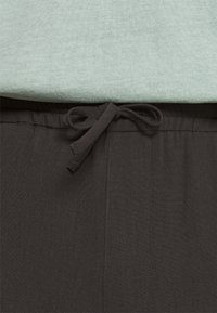 Pantalon noir avec une taille à cordon de serrage, présentant une texture lisse et une brillance subtile, associé à un t-shirt à manches courtes côtelé de couleur vert clair.