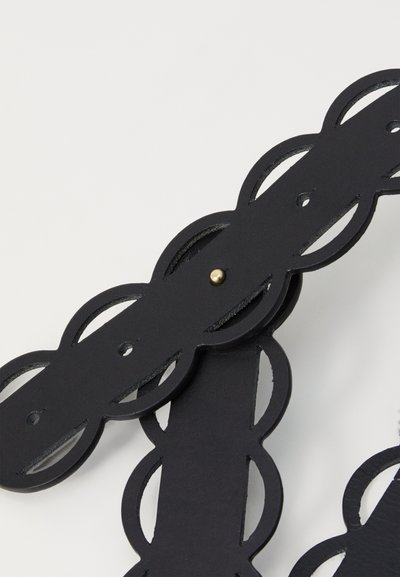 Black leather strap featuring a cut-out design with interconnected oval shapes and a gold-tone stud accent. Smooth texture and matte finish.
