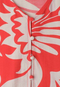 Tissu à motif floral rouge et blanc avec des boutons recouverts de tissu courant sur le devant central d’un vêtement.