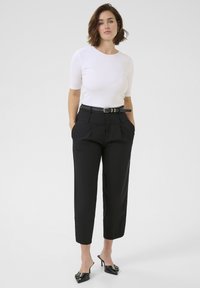 Black tailored pants with pleats, worn with a fitted white ribbed top. Black belt with silver buckle, paired with black heeled mules.