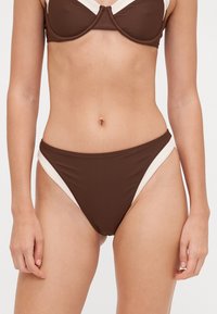 Brūns bikini top ar strukturētu dizainu, ar krēmkrāsas sānu akcentiem; atbilstoši brūni bikini apakšdaļas ar kontrastējošiem krēmkrāsas elementiem.