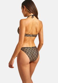 Maillot de bain en noir et or avec motif. Design à col halter ; bas taille basse avec imprimé géométrique ; texture lisse ; matériel minimal.