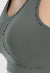 Sostén en un tejido verde apagado con una textura suave, con escote redondo y tirantes anchos, diseñado para brindar comodidad y soporte.