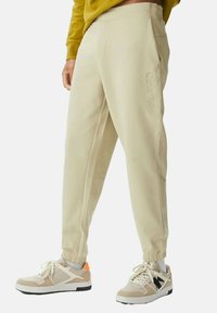 Pantalones de chándal beige con puños elásticos que cuentan con un bolsillo lateral y una marca en relieve de "Calvin Klein". Combinados con zapatillas beige y blancas.
