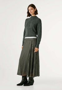 Maglione grigio a maglia con collo alto, abbinato a una lunga gonna a scacchi bianca e nera. Il modello indossa stivaletti neri con tacco. Design semplice.