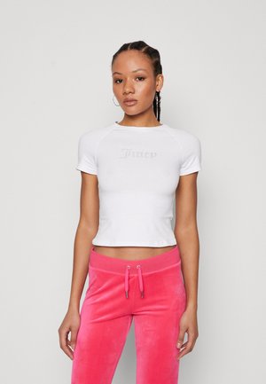 T-shirt blanc court avec des manches raglan courtes et "Juicy" en strass sur le devant, associé à un jogging en velours rose avec une taille à cordon.