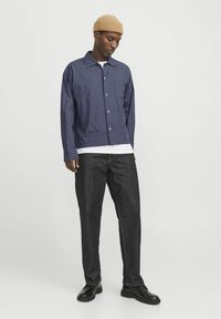 Marineblå og hvid ternet skjorte med knapper, parret med mørk denim bukser og sorte sko. Skjorten har spredt krave og lange ærmer.
