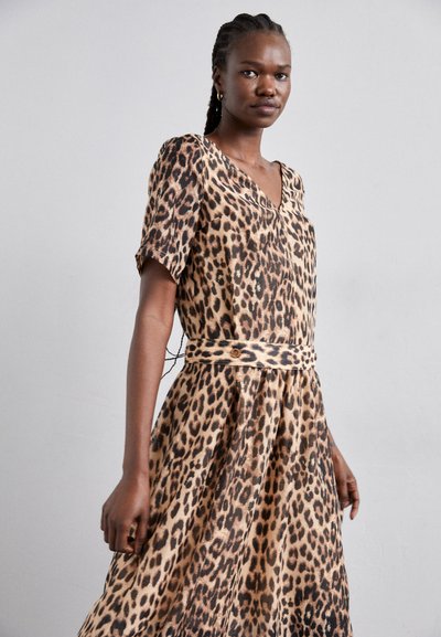 Robe imprimée léopard avec décolleté en V, manches courtes et taille nouée. Tissu léger avec une silhouette fluide. Les couleurs brunes et beiges dominent.