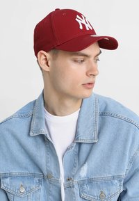 Burgundi baseball sapka fehér "NY" logóval, textilből készült, ívelt szárral. Világoskék farmerdzsekivel viselve.