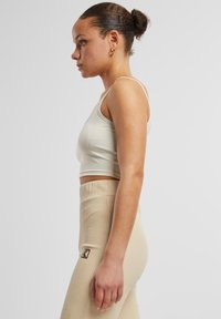 Svetlo béžový skrátený top s tenkými ramienkami, doplnený béžovými rebrovanými legínami s vysokým pásom, na ktorých je malá nášivka na boku.