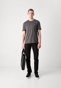 Šedé bavlnené tričko, výstrih do V, krátke rukávy; čierne džínsy; čierne tenisky s krémovou podrážkou; drží elegantnú čiernu tašku.