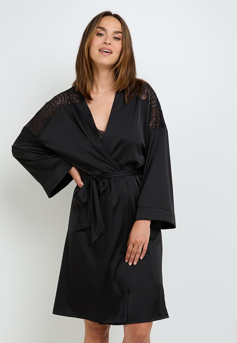 Robe en satin noir avec des détails en dentelle sur les épaules, conception enroulée et ceinture à nouer. Manches évasées et coupe au genou. Texture lisse.