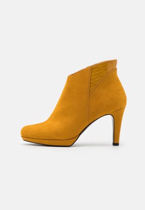 Ankelstøvle i sennepsgul ruskind med en 3-tommer stiletthæl og krokodillepræget læderdetalje bagpå.