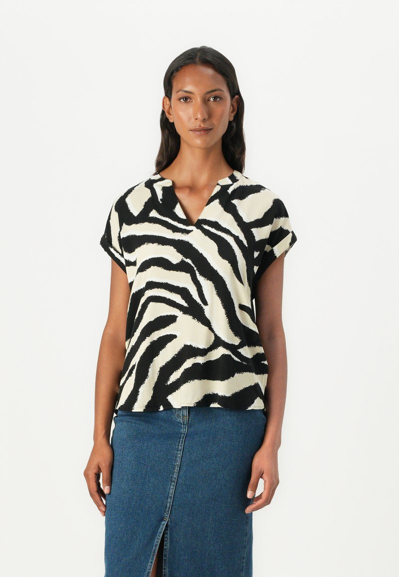 Blouse à rayures zèbres noir et crème à manches courtes, avec un décolleté en V et une coupe ample, associée à une jupe en denim avec une fente sur le devant.