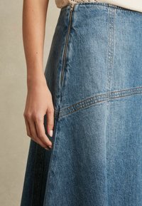 Lichtblauwe denim midi-rok met een zijrits, zichtbare stiksels en een uitlopende snit. De textuur lijkt zacht en heeft een gemiddeld gewicht.