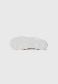 Semelle de sneaker blanche avec une surface en caoutchouc texturée, des motifs circulaires et des bords striés. Logo embossé près du talon. Design épuré et minimal.