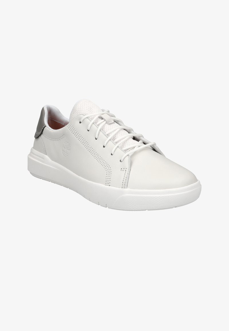 Biele kožené tenisky s mesh jazykou a šedým detailom na päte. Obsahujú okrúhlu špičku, šnurovanie a textúrovanú gumovú podrážku.
