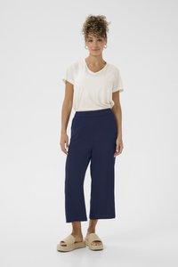 T-shirt crème à col en V associé à un pantalon large bleu marine. La tenue est agrémentée de sandales à plateforme tressées beiges avec une finition texturée.