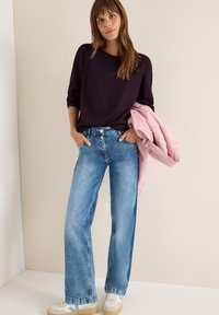Mørk lilla langærmet top, lys blå bred ben jeans og en lys pink jakke. Hvite sneakers med blå accenter. Glatte stofoverflader.