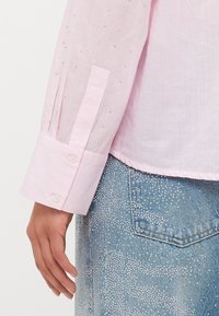 Pink striped long-sleeve shirt with shiny embellishments on the sleeves, featuring white buttons on the cuff and a smooth fabric texture.