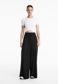 T-shirt bianco cropped con arricciatura frontale e maniche corte, abbinato a pantaloni neri a gamba ampia a vita alta con coulisse.