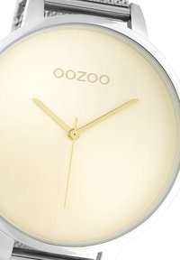 Montre en maille en acier inoxydable argenté avec un boîtier rond poli, dotée d'un cadran doré clair, d'aiguilles dorées et du logo "OOZOO" imprimé.