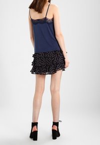 Navy camisole met kantafwerking gecombineerd met een zwarte rok met ruffles en een bloemenpatroon. Het modele draagt zwarte hoge hakken sandalen.