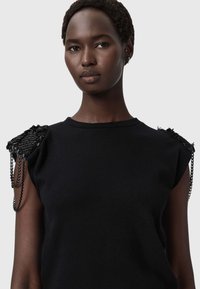 Czarny dzianinowy top z ozdobnymi akcentami na ramionach, teksturowaną tkaniną, łańcuszkowymi zdobieniami i klasycznym okrągłym dekoltem.