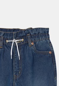 Džínové kraťasy s elastickým pasem na šňůrku, modré barvy, měděné akcenty na kapsách a kartáčovanou strukturou.