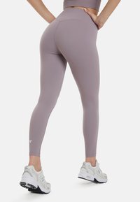 Lys lilla leggings med høj talje og glat tekstur, parret med hvide træningssko med grå detaljer.