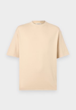 Bézs színű, bővített szabású, rövid ujjú póló kerek nyakkivágással és minimális varrással, világosszürke háttéren.