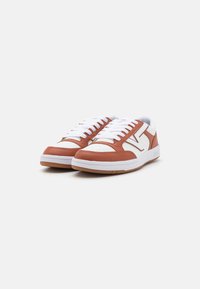 Brune og hvite lær sneakers med flat design, med hvite snørebånd, teksturert overdeler og en gummisåle med en kontrasterende aksent.