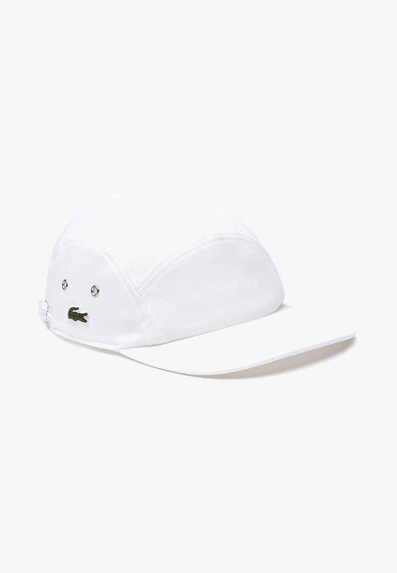 Witte pet met een afgeronde top en een korte rand, gemaakt van textuurstof. Heeft een klein groen krokodillenlogo aan de zijkant.