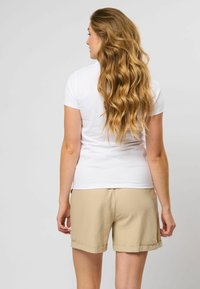 Witte T-shirt met korte mouwen, gecombineerd met lichtbeige shorts met opgerolde cuffs. Glad stofoppervlak zichtbaar.