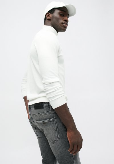 Λευκό πλεκτό πουλόβερ με πλεχτά μανίκια και όρθιο γιακά, συνδυασμένο με σκούρες γκρίζες στενές τζιν παντελόνες που διαθέτουν πίσω τσέπες και διακριτική επωνυμία.