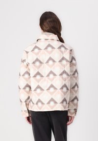 Κοντό μπουφάν με γεωμετρικό σχέδιο σε μπεζ, Ρ�οζ και καφέ αποχρώσεις. Σημαντικές λεπτομέρειες περιλαμβάνουν κλασικό γιακά και μακριά μανίκια.