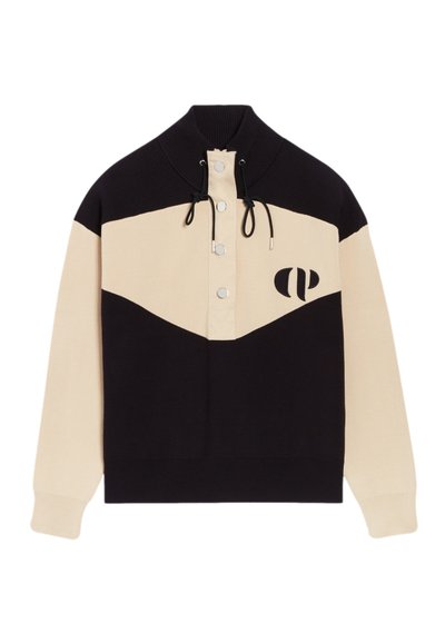 Pull-over coloré avec un col haut, présentant des sections noires et beiges. Inclut des boutons pression et un accent de logo sur la poitrine.