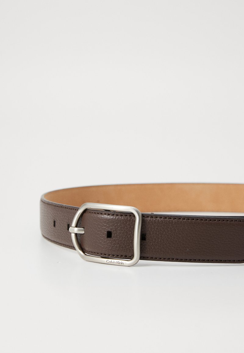 Ceinture en cuir marron avec une finition texturée, une boucle rectangulaire en argent et des trous uniformément espacés pour un ajustement.