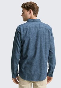 Heren overhemd met lange mouwen van donkerblauwe textuurstof. Voorzien van een button-down kraag, mouwen met knopen en een rechte zoom.