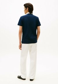 Polo de color azul marino con mangas cortas, cuello blanco en contraste, combinado con pantalones blancos y zapatos negros. Textura de tela suave.