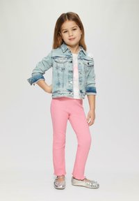 Veste en denim avec 2 poches poitrine, t-shirt blanc avec texte rose, pantalons rose côtelés avec manchons volants, et chaussures plates argentées métalliques.