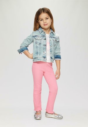 Denim jacket met 2 borstzakken, wit T-shirt met roze tekst, roze geribbelde broek met ruffles aan de mouwen, en metallic zilveren platte schoenen.