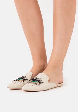 Mocassins beiges à dos ouvert, ornés d'un motif d'œil décoré de perles et d'accents métalliques. Semelle plate, forme à bout pointu.