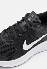 Zwarte sportschoen met een bovenwerk van mesh, textuurnuances, versterkte veteroogjes en een contrasterend wit Nike-swooshlogo.